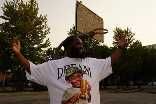 Person wearing a white t-shirt with a graphic design of a child holding a trophy and the word 'Dream'.
