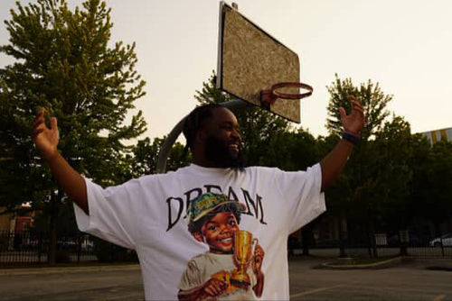 Person wearing a white t-shirt with a graphic design of a child holding a trophy and the word 'Dream'.